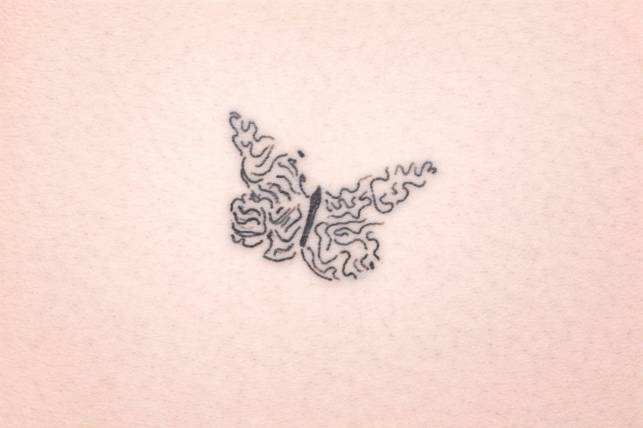 Filigranes Fine-Line-Tattoo eines Schmetterlings aus geschwungenen Linien auf Tattoo-Kunsthaut.