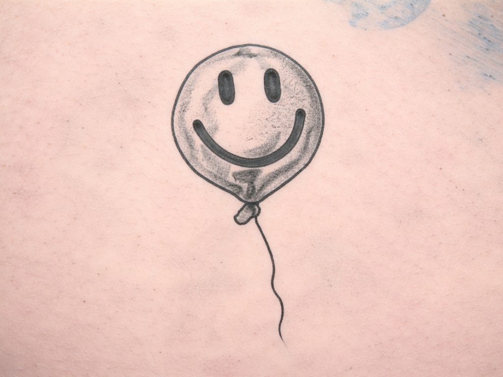 Schwarz-graues Tattoo eines Smiley-Ballons mit dünner Schnur auf Tattoo-Kunsthaut.